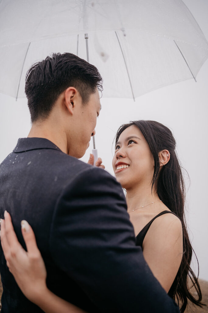 Couple embraces under transparent umbrella.