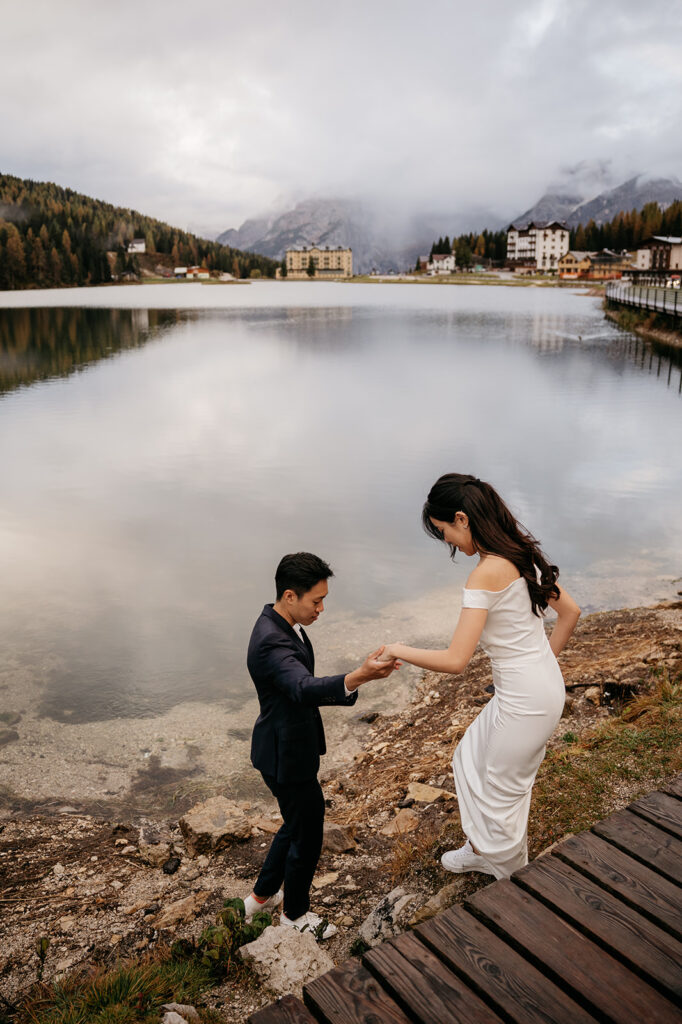 Couple by mountain lake in elegant attire.