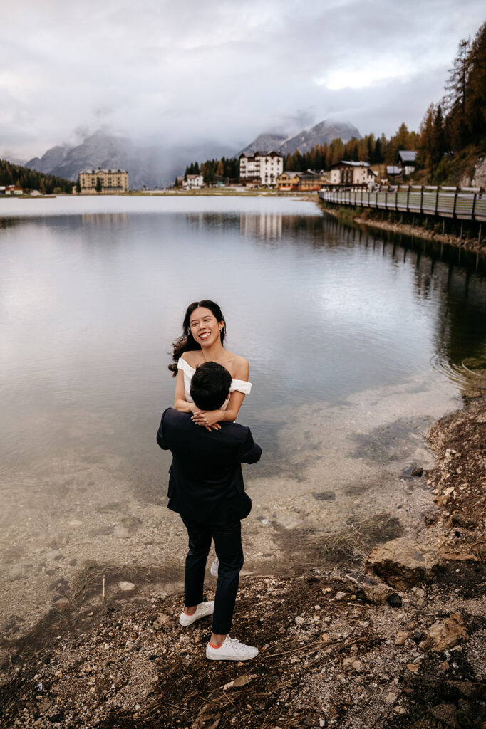 Couple embracing by a mountain lake, cloudy day.