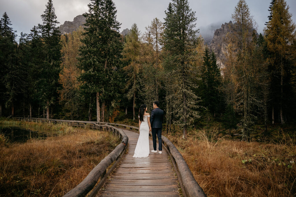 Bride and groom walk on forest boardwalk.