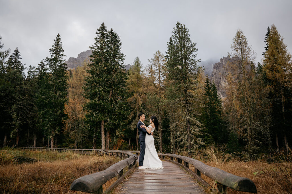 Couple embraces on forest bridge for wedding photo.