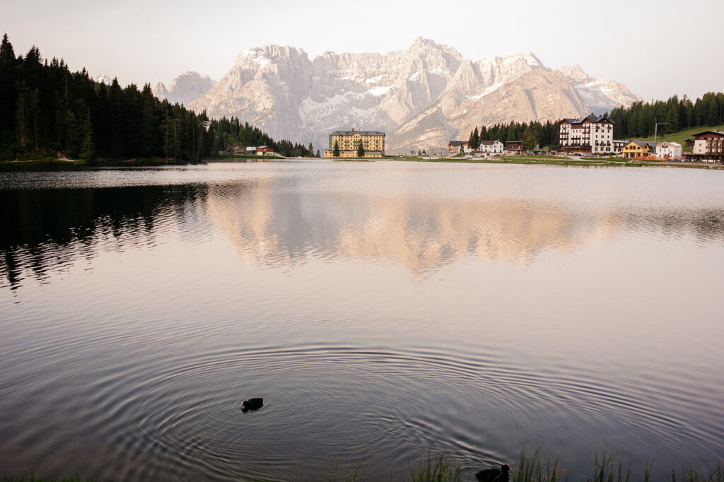 Mountain lake reflecting peaks and buildings at sunset.