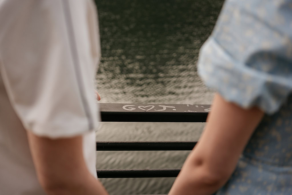 Couple standing by river, holding hands.