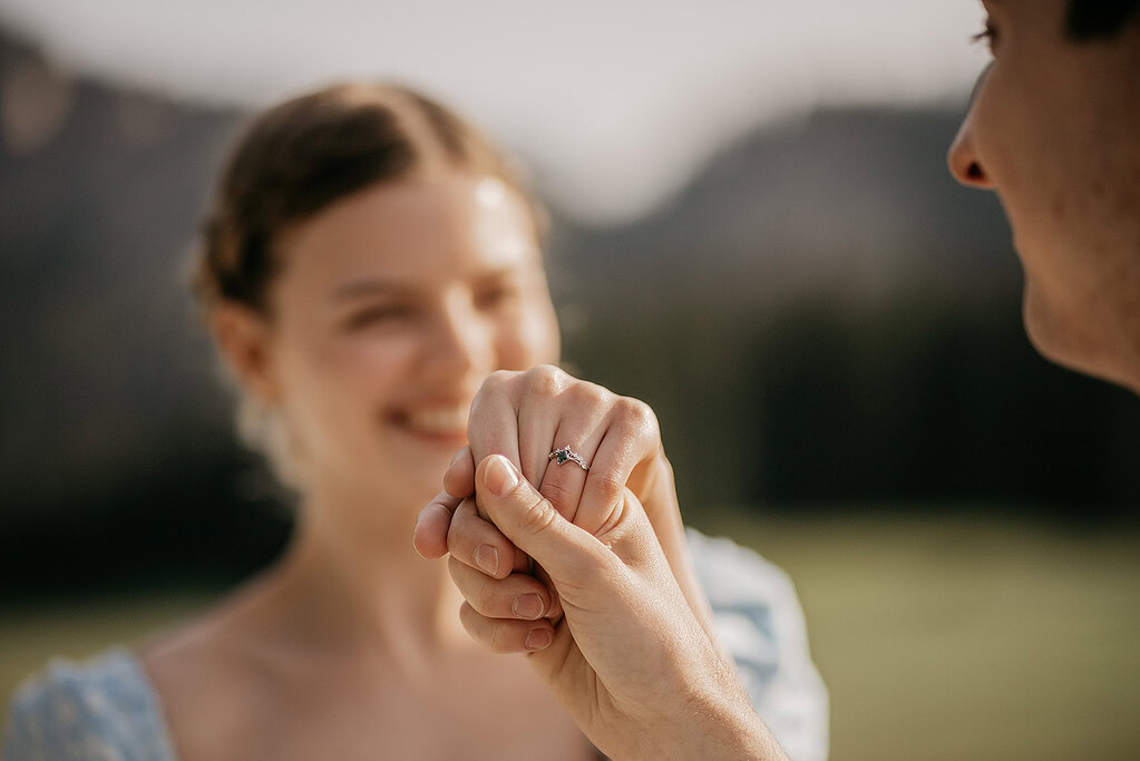 Couple holding hands with engagement ring visible.