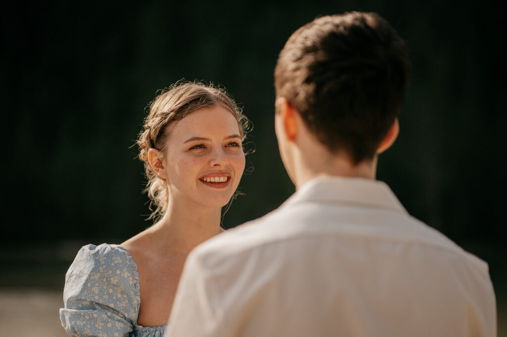 Smiling woman facing man outdoors, sunny day.