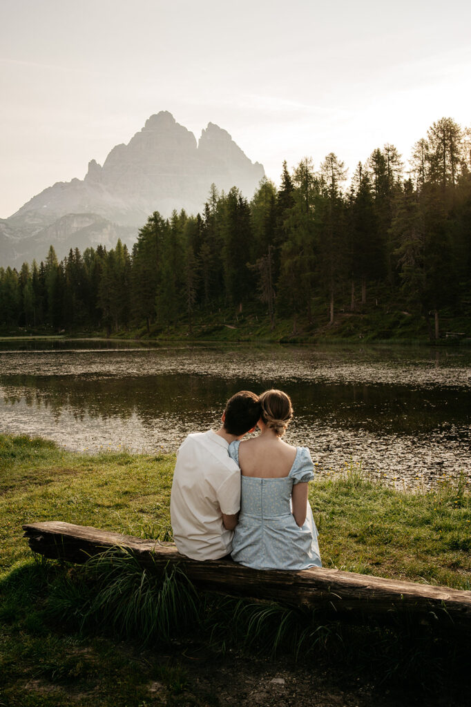 Couple sitting by lake, forest and mountains view.