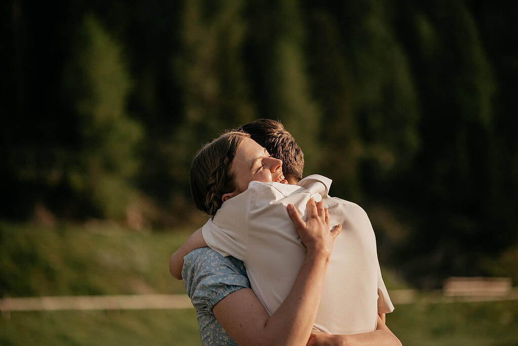 Couple embracing outdoors with trees in background.