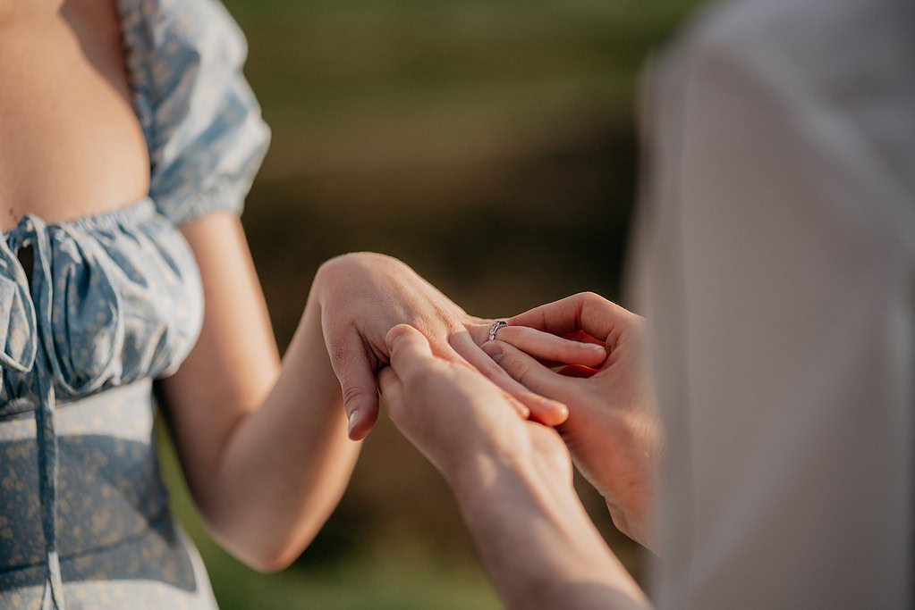 Person placing ring on another's finger during proposal.