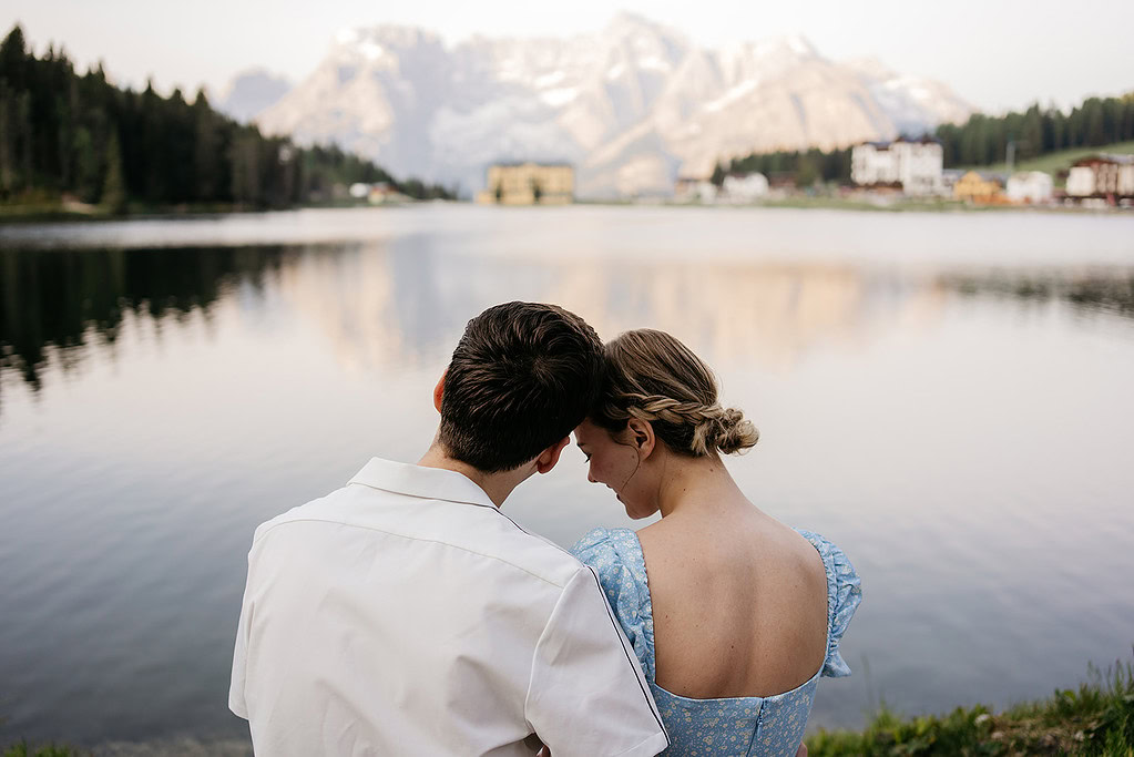 Couple by mountain lake, embracing peacefully.