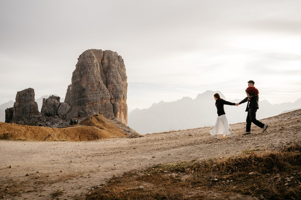 Couple walking on mountain path, bouquet of roses