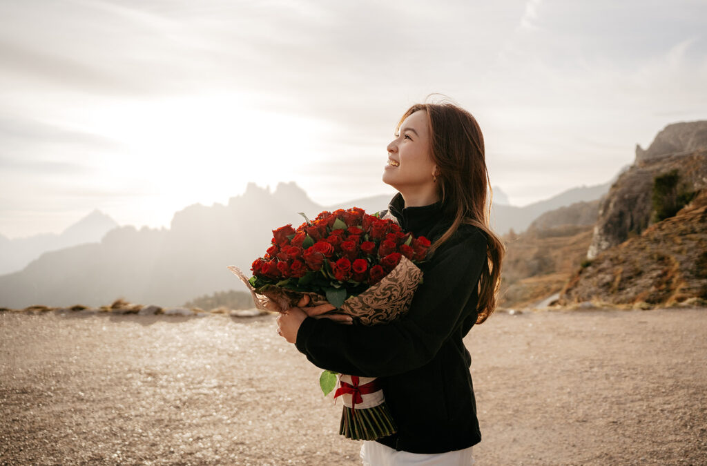 Woman smiling, holding bouquet of red roses outdoors.