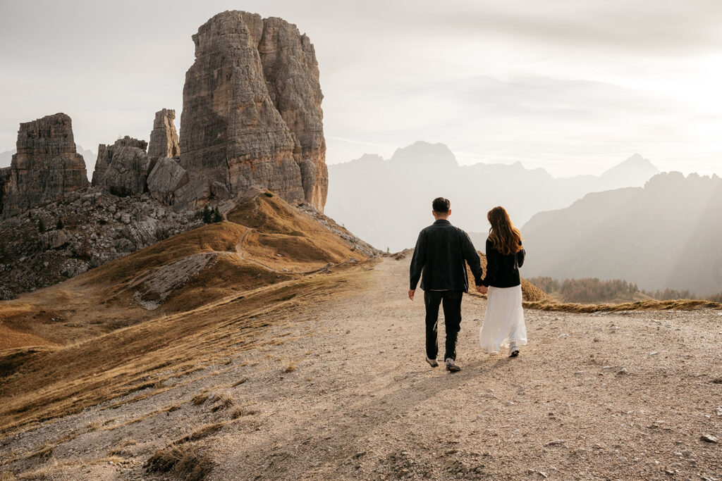 Couple holding hands walking towards scenic mountain view.