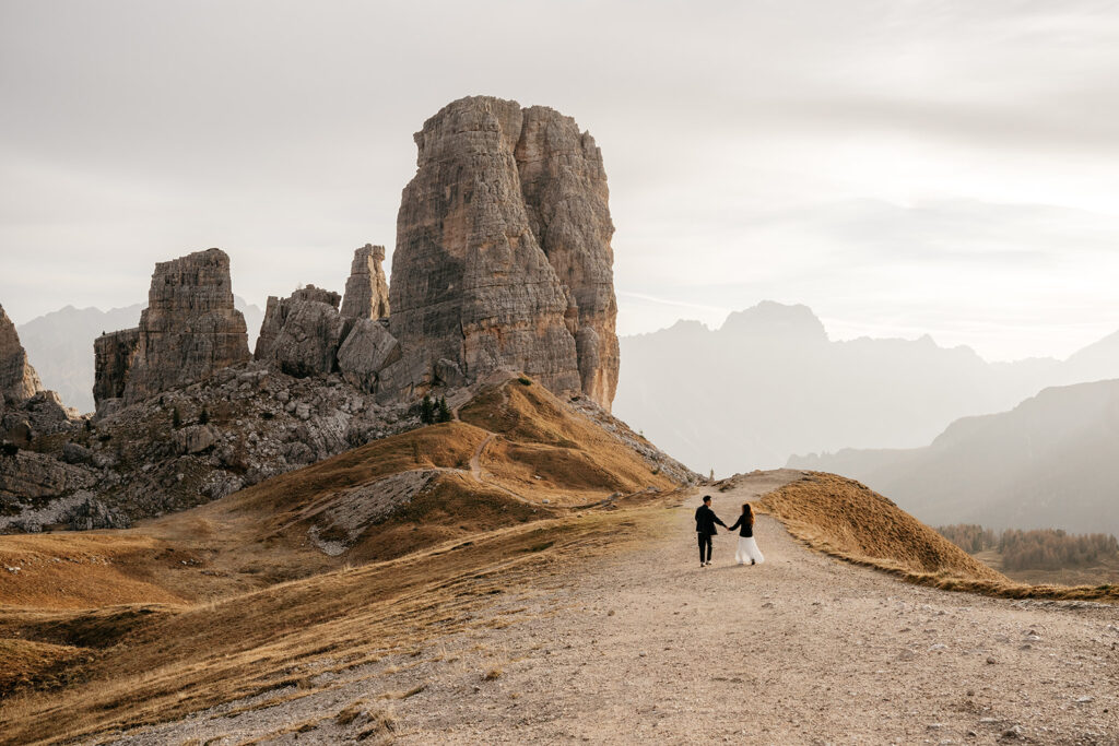 Couple walks on mountain path, rocky peaks background.