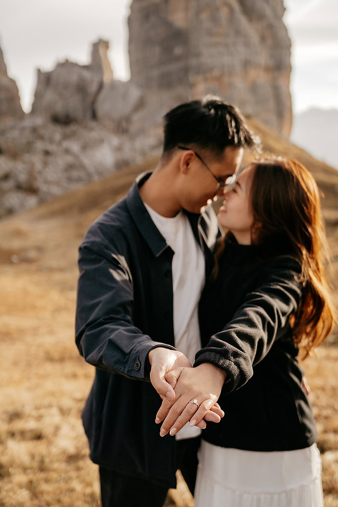 Couple embracing outdoors with engagement ring visible.