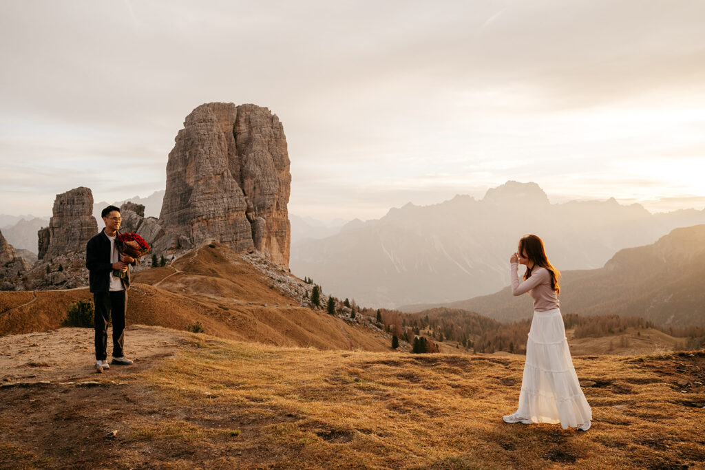 Couple in mountains, man with flowers, romantic moment.