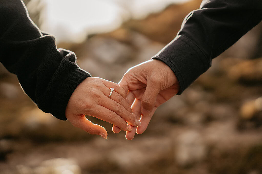 Couple holding hands, engagement ring visible.