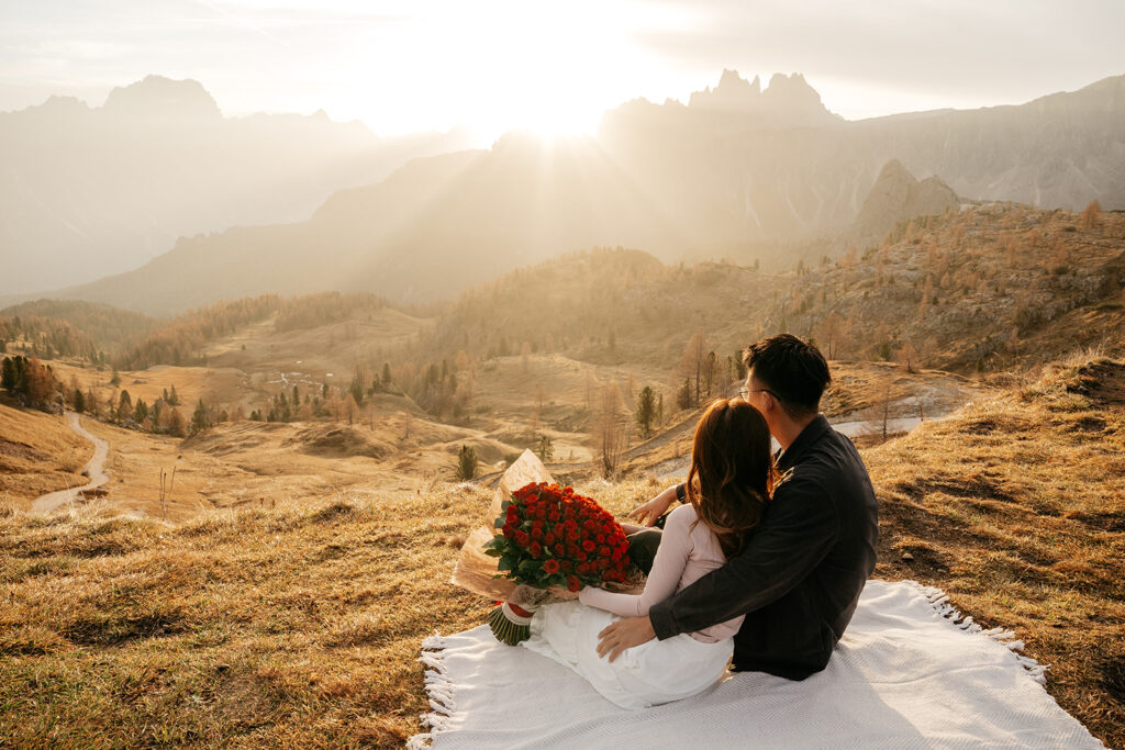 Couple embracing with roses at sunset in mountains.