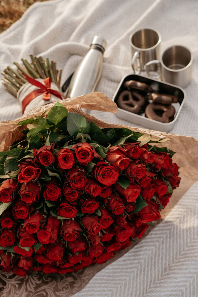 Bouquet of red roses and picnic items on blanket.