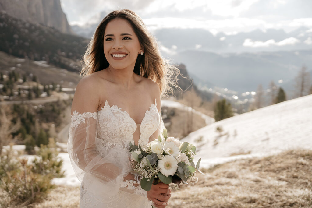 Bride in lace dress holding floral bouquet outdoors.