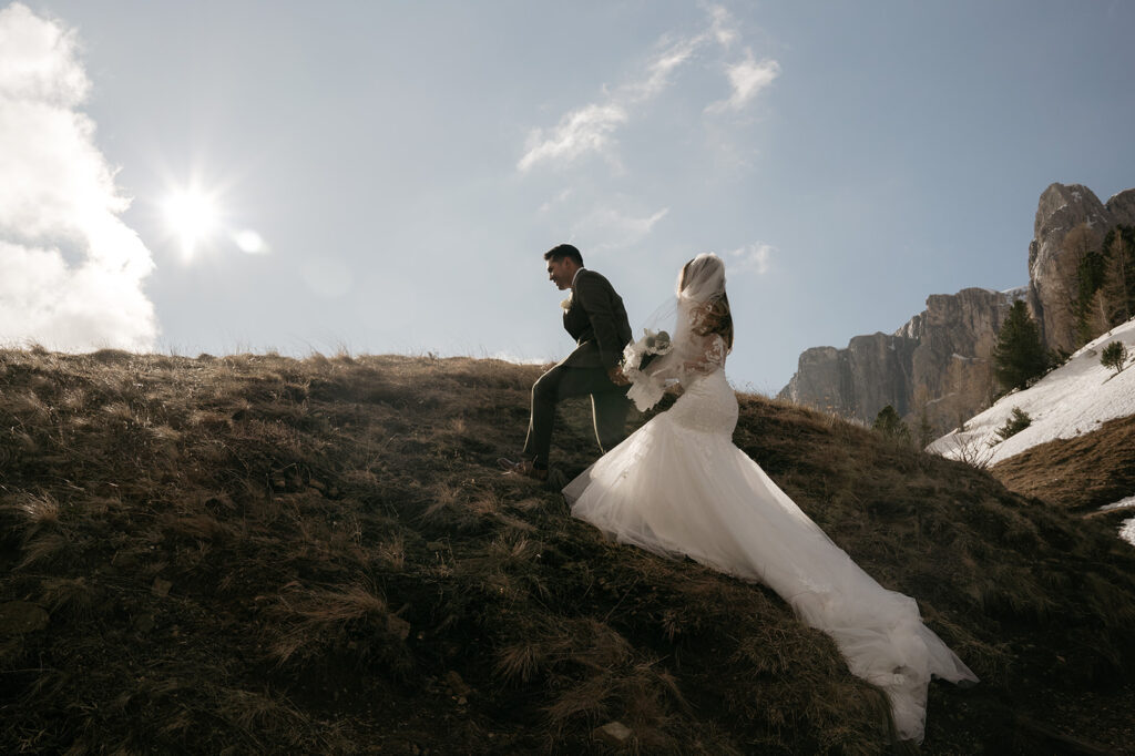 Bride and groom hiking mountain in wedding attire.