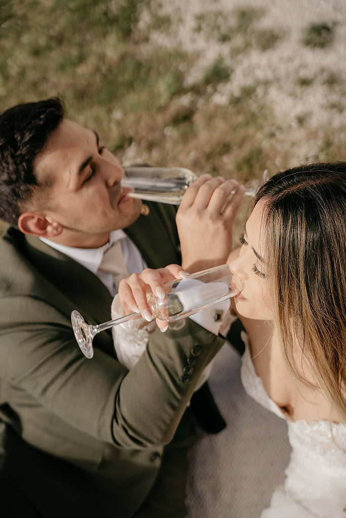 Couple drinking champagne outdoors in wedding attire.