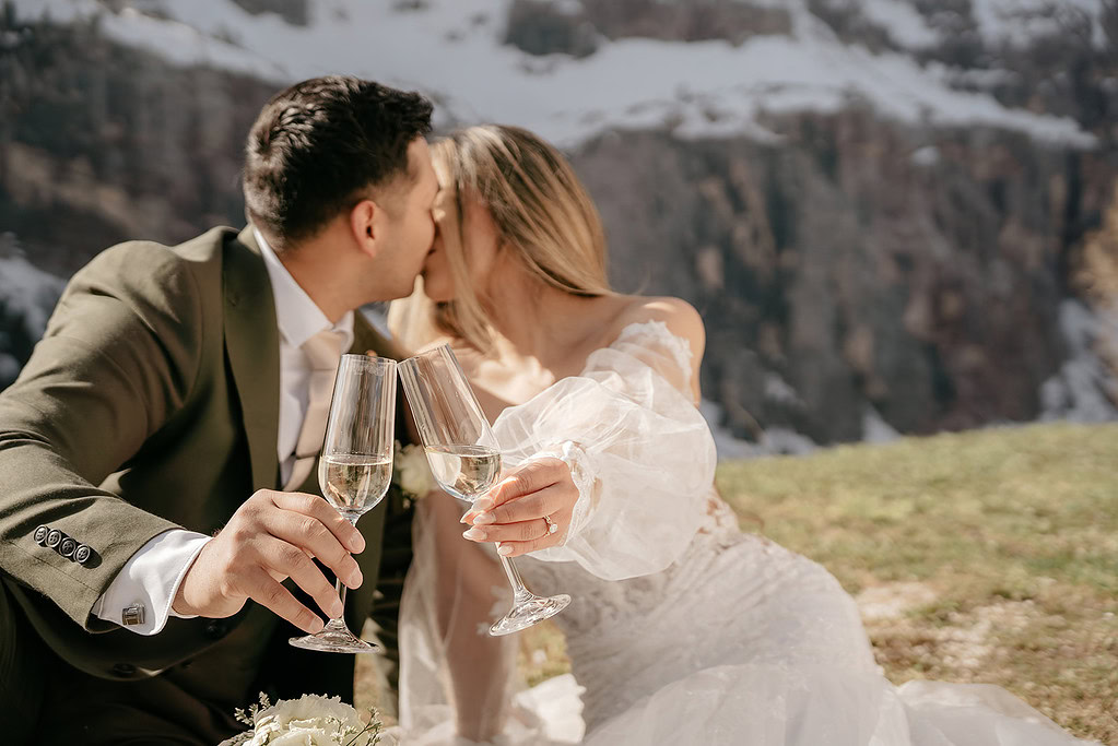 Couple kissing outdoors, toasting with champagne glasses.