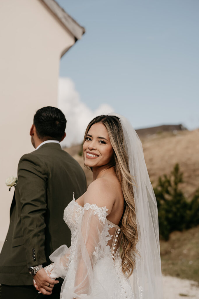 Happy bride holding groom's hand outdoors.