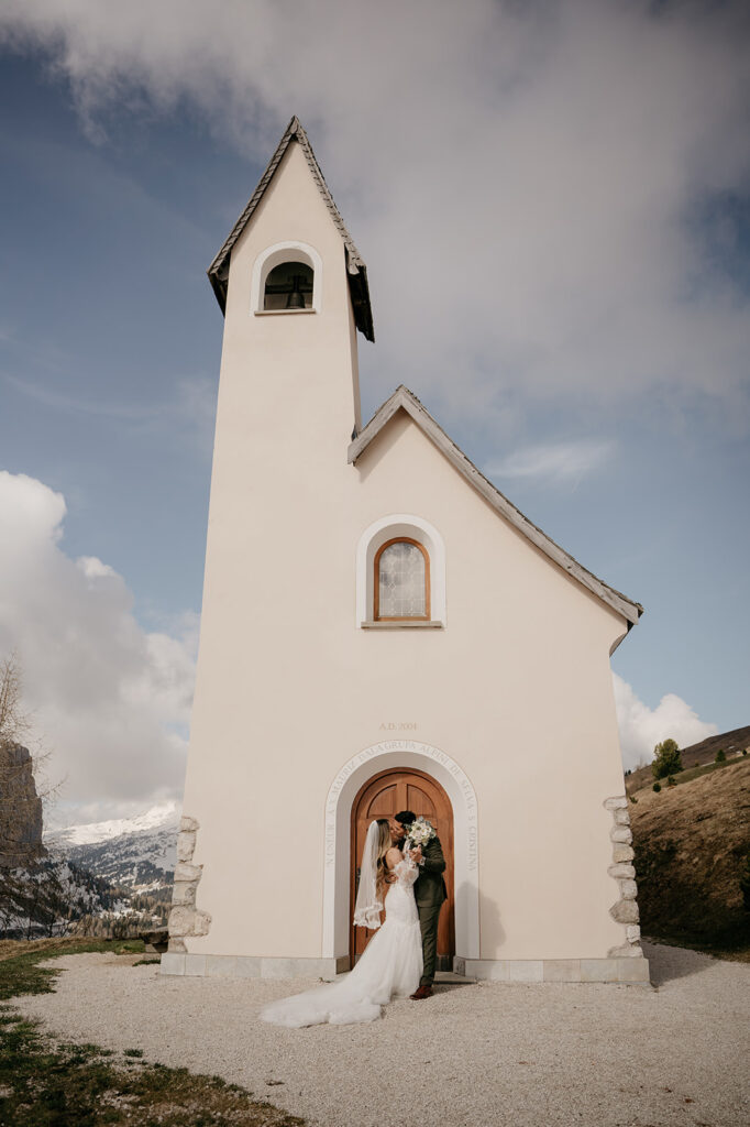 Bride and groom kissing outside small chapel