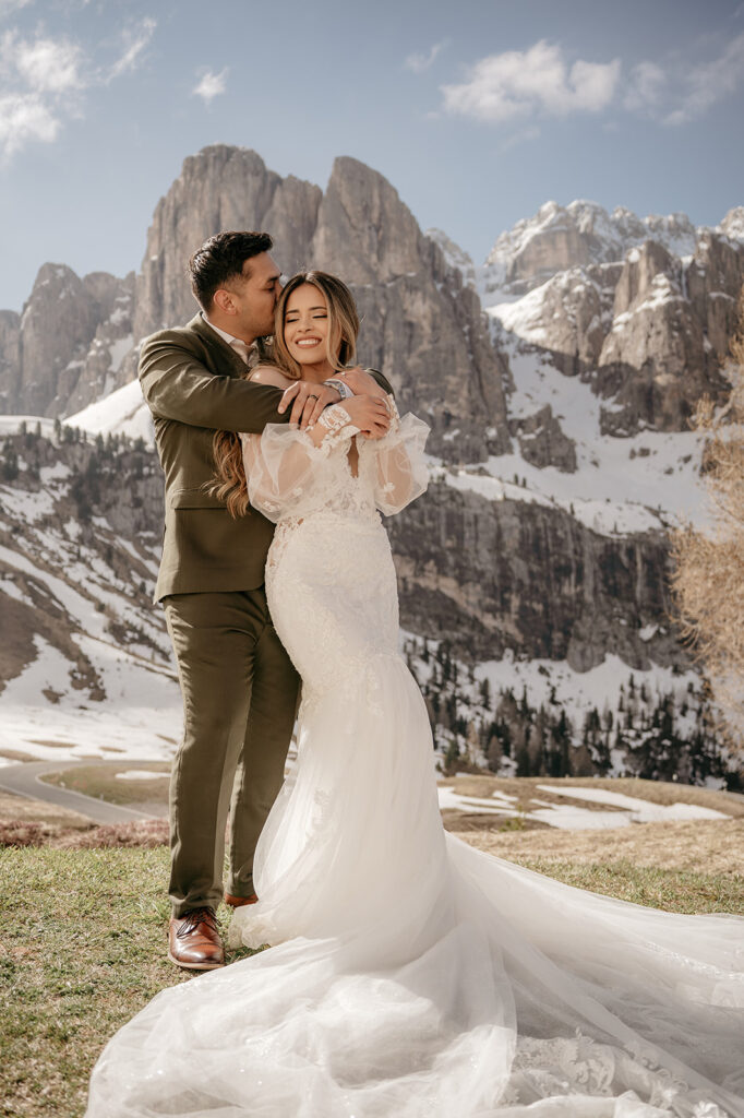 Bride and groom embracing in snowy mountain landscape.