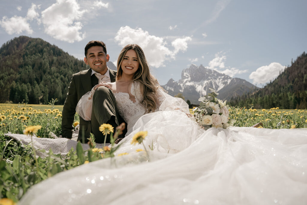 Bride and groom sitting in mountain meadow.