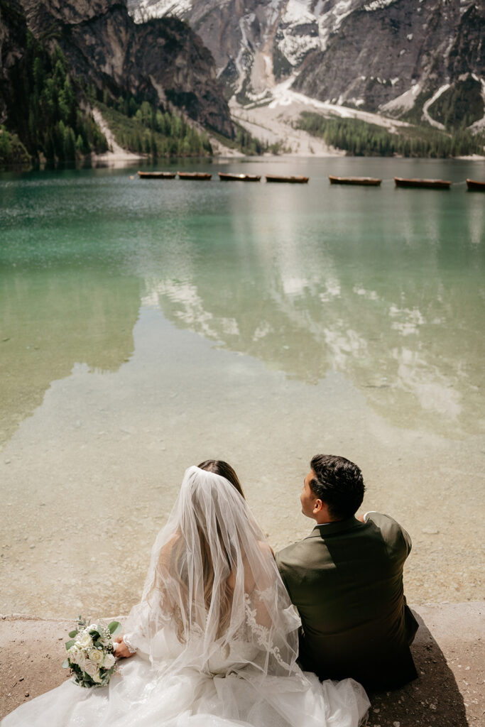 Bride and groom sit by a serene lake.