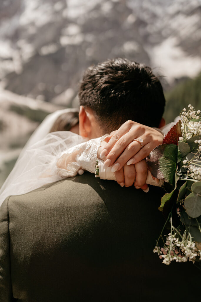 Bride embraces groom with bouquet, mountain background.