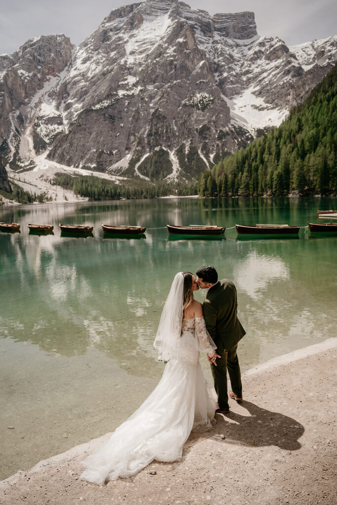 Bride and groom kissing by mountain lake.