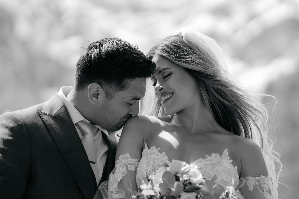 Bride smiling, groom kissing her shoulder.