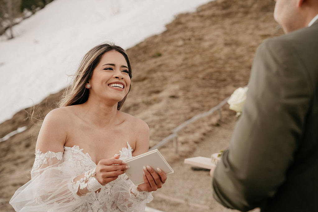 Bride smiling, holding vows in snowy landscape.