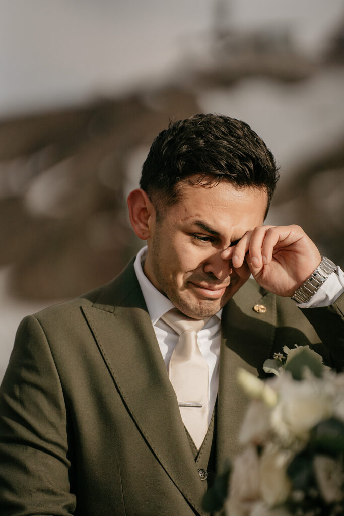 Emotional groom wiping tears at wedding ceremony.