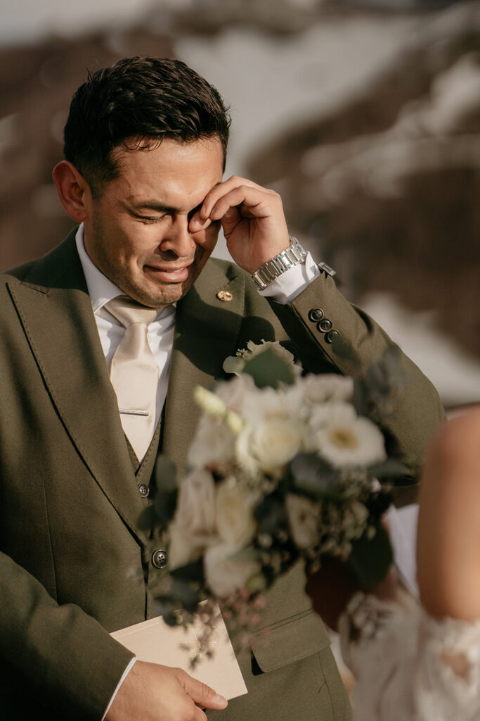 Man wipes tear during emotional outdoor wedding ceremony.