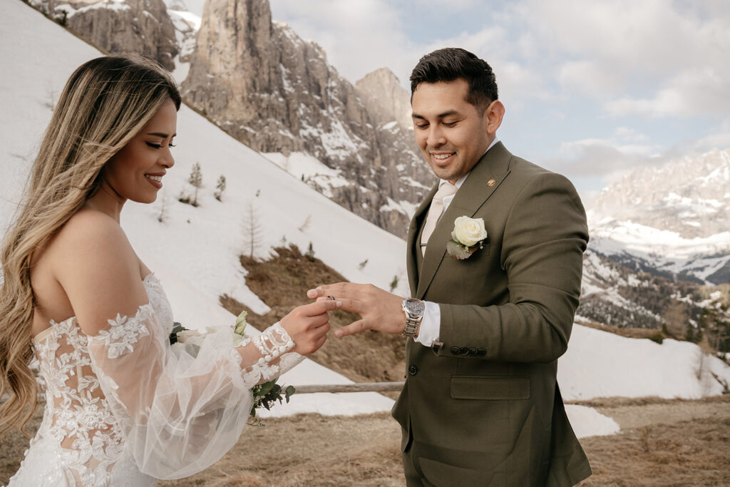 Bride and groom exchanging rings, snowy mountain backdrop.