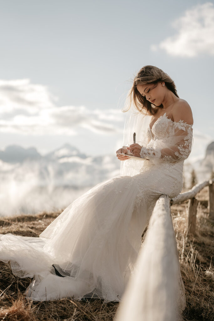 Bride in lace gown writing on notepad outdoors