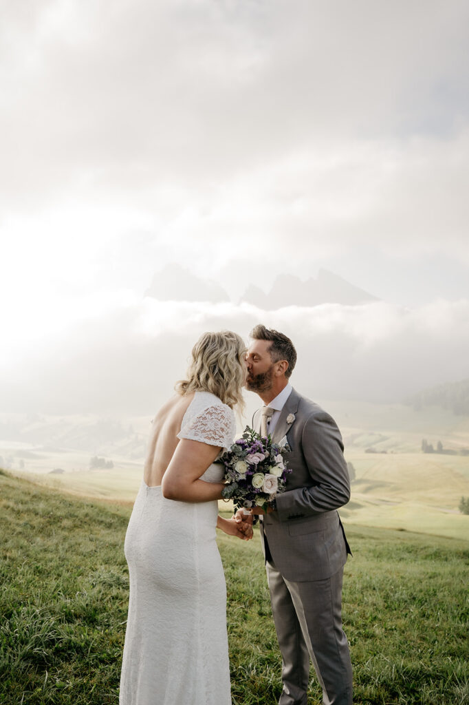 Bride and groom kiss in scenic outdoor setting.