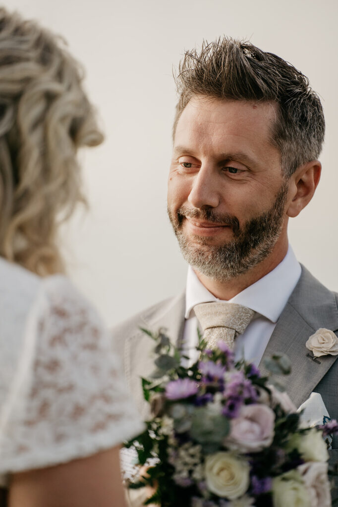 Groom smiling at bride with bouquet