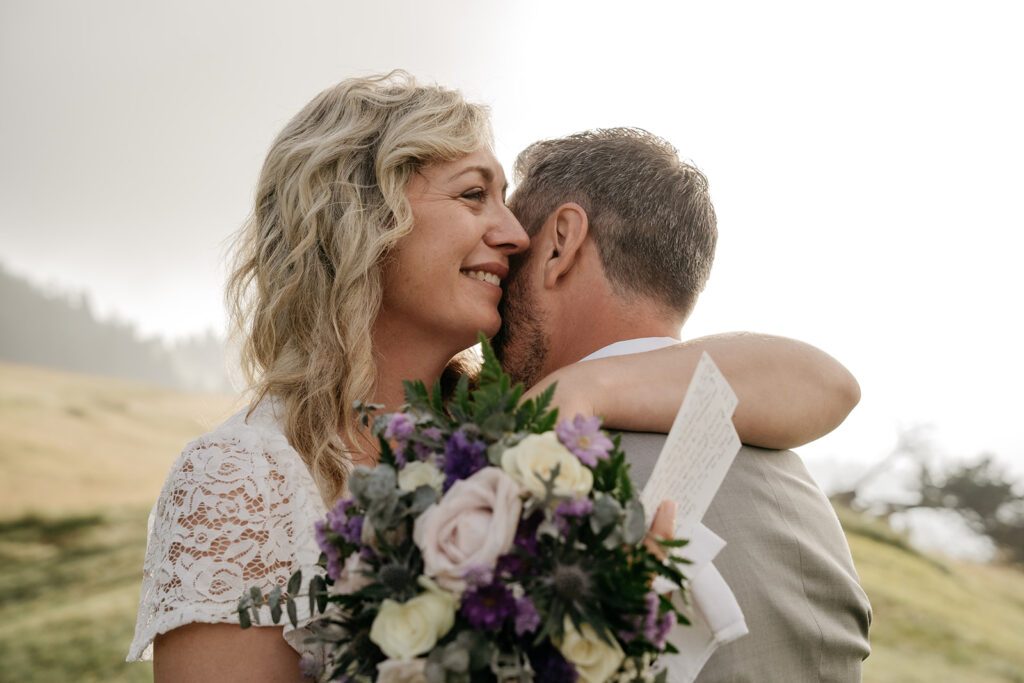 Couple embraces outdoors with bouquet and letter.