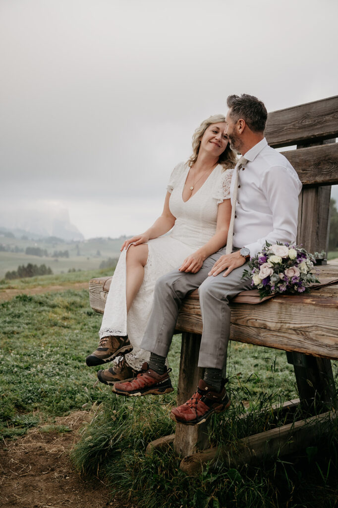 Couple sitting on wooden bench outdoors, smiling.