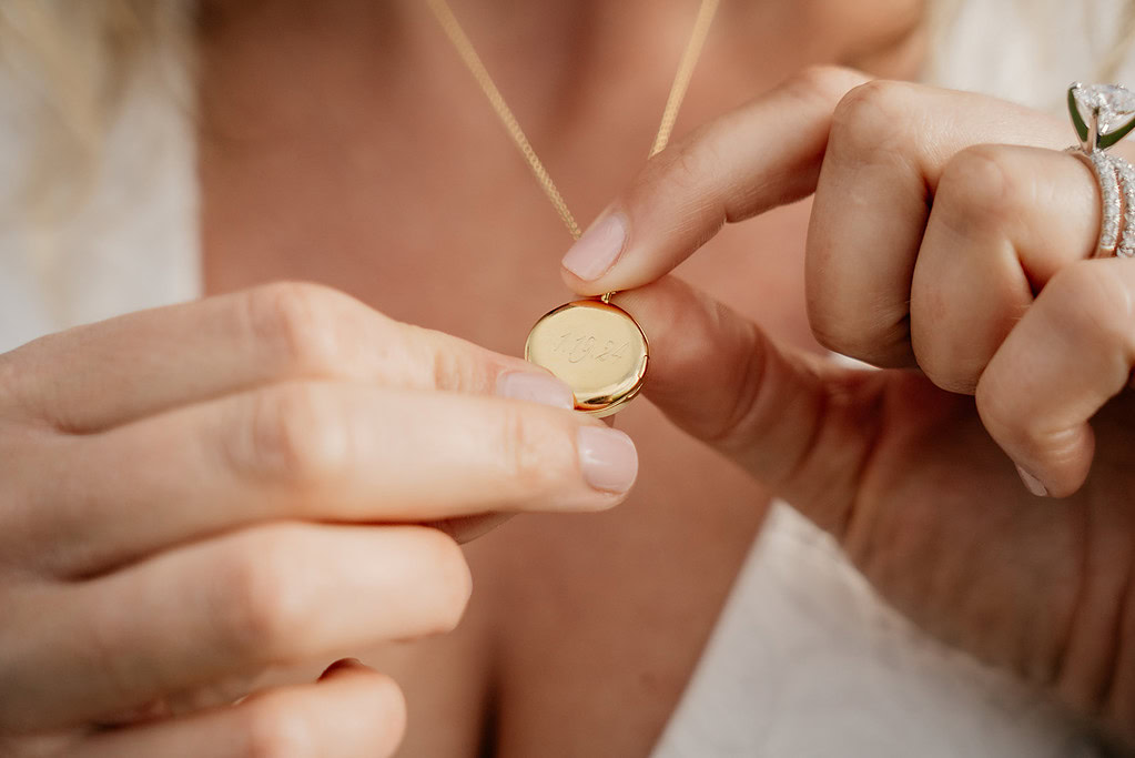 Close-up of hands holding engraved gold locket necklace