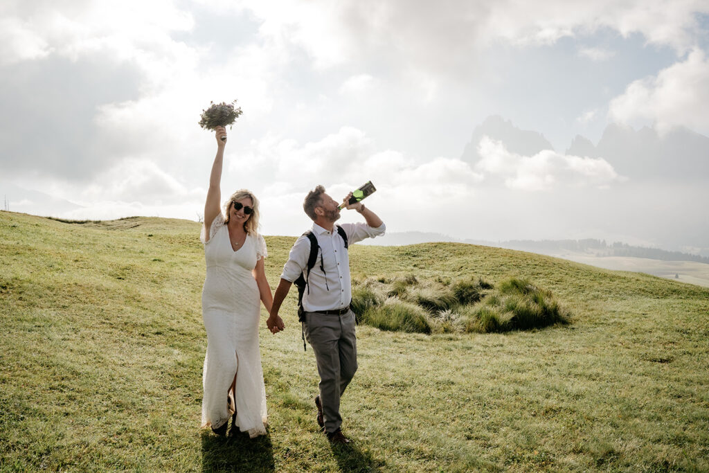 Couple celebrating outdoors with bouquet and drink.