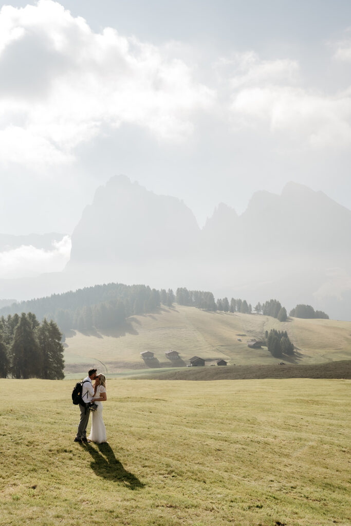 Couple standing in a grassy field with mountains.