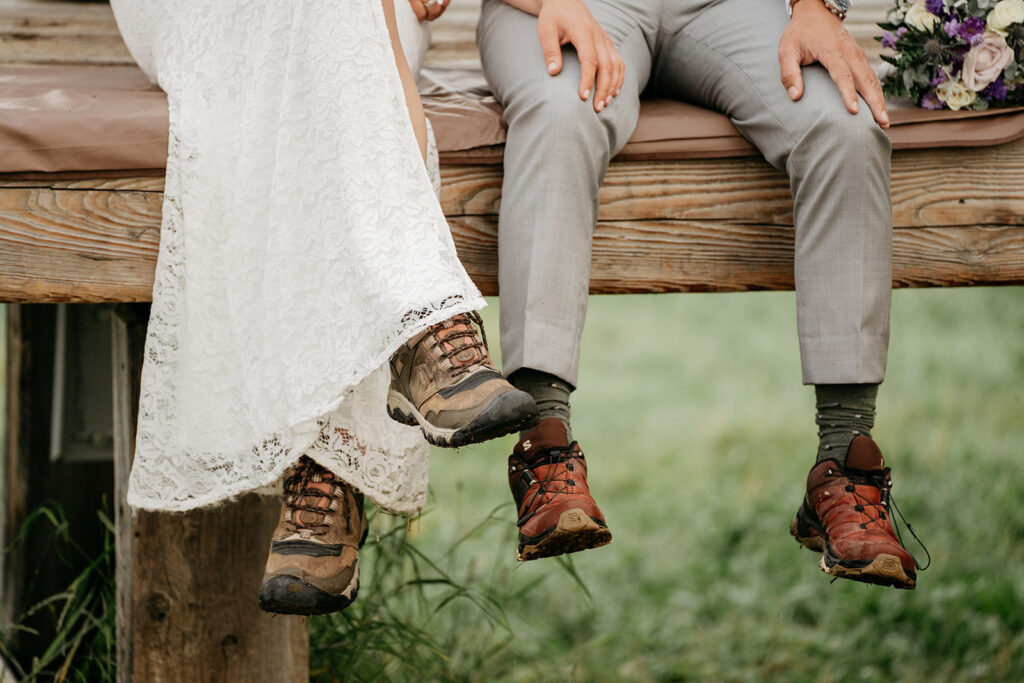 Bride and groom in hiking boots on wood ledge.