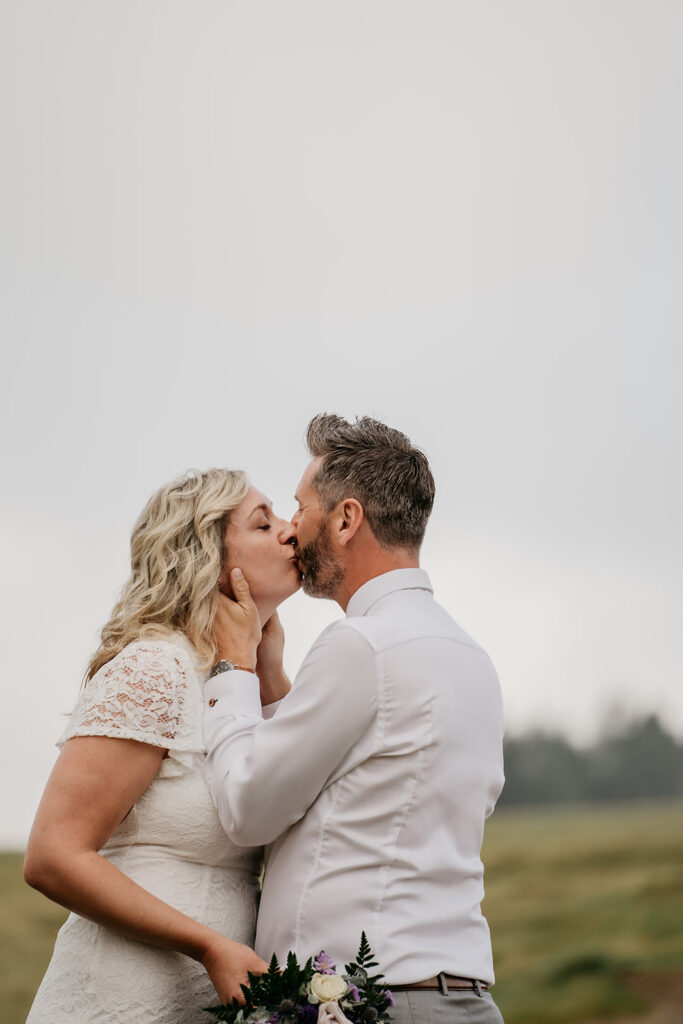 Couple kissing outdoors, bride holding bouquet.