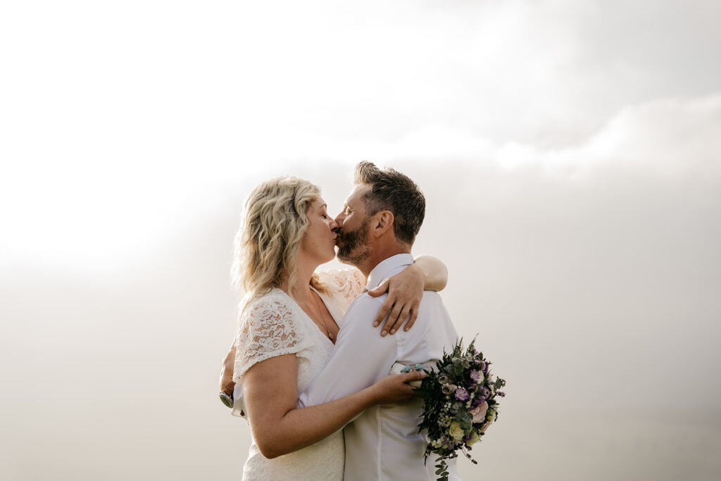 Couple kissing outdoors holding flowers.