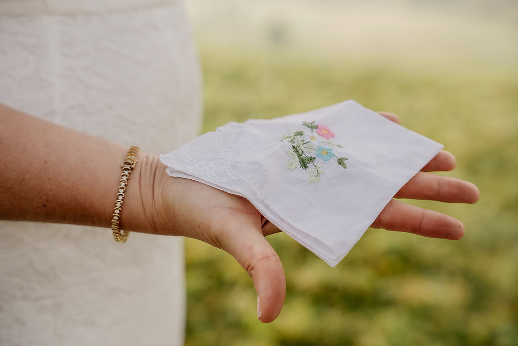 Hand holding embroidered white handkerchief outdoors.